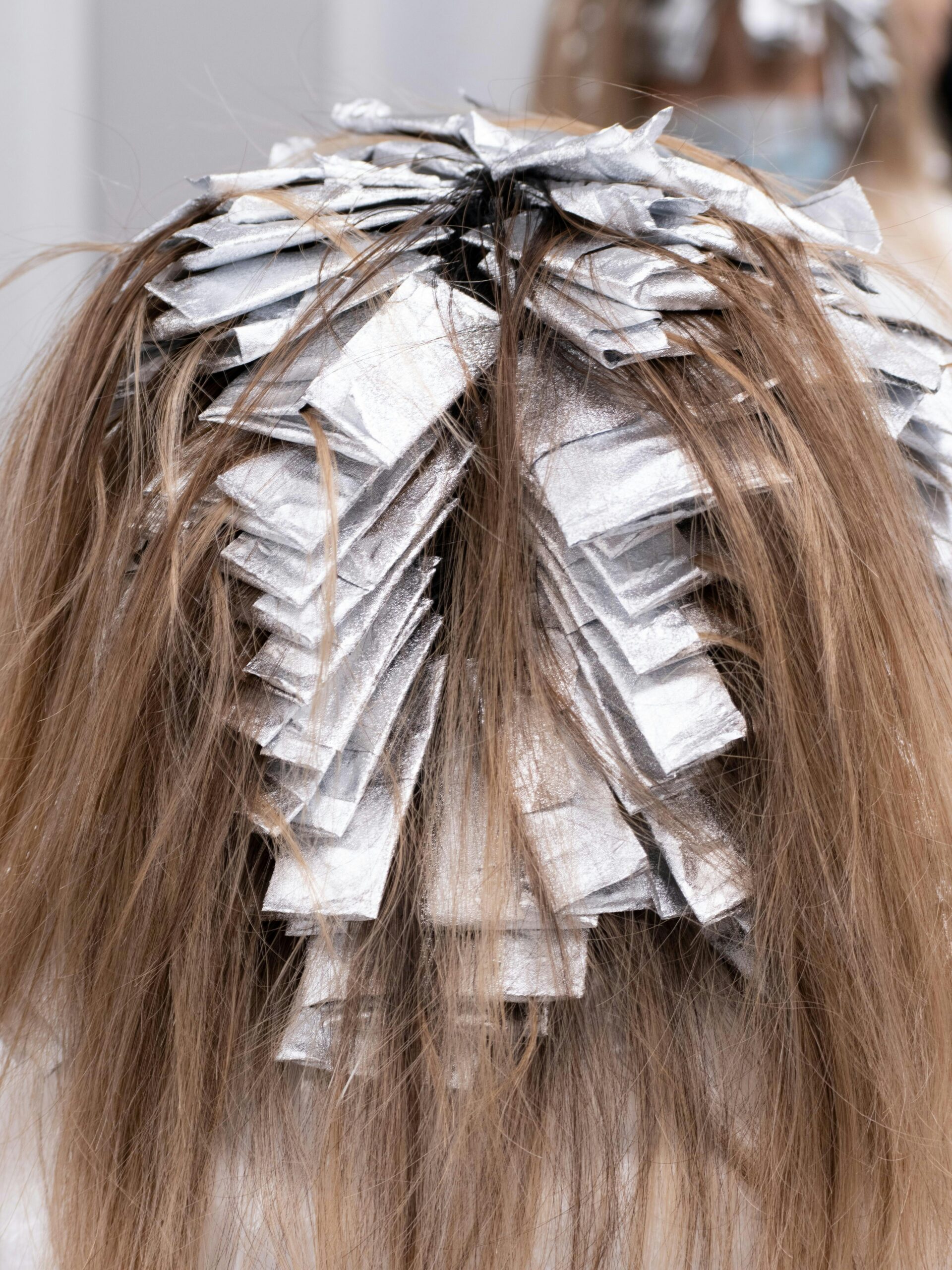 Arrière de la tête d’une cliente avec des papillotes, en plein soin de coloration partielle chez le coiffeur