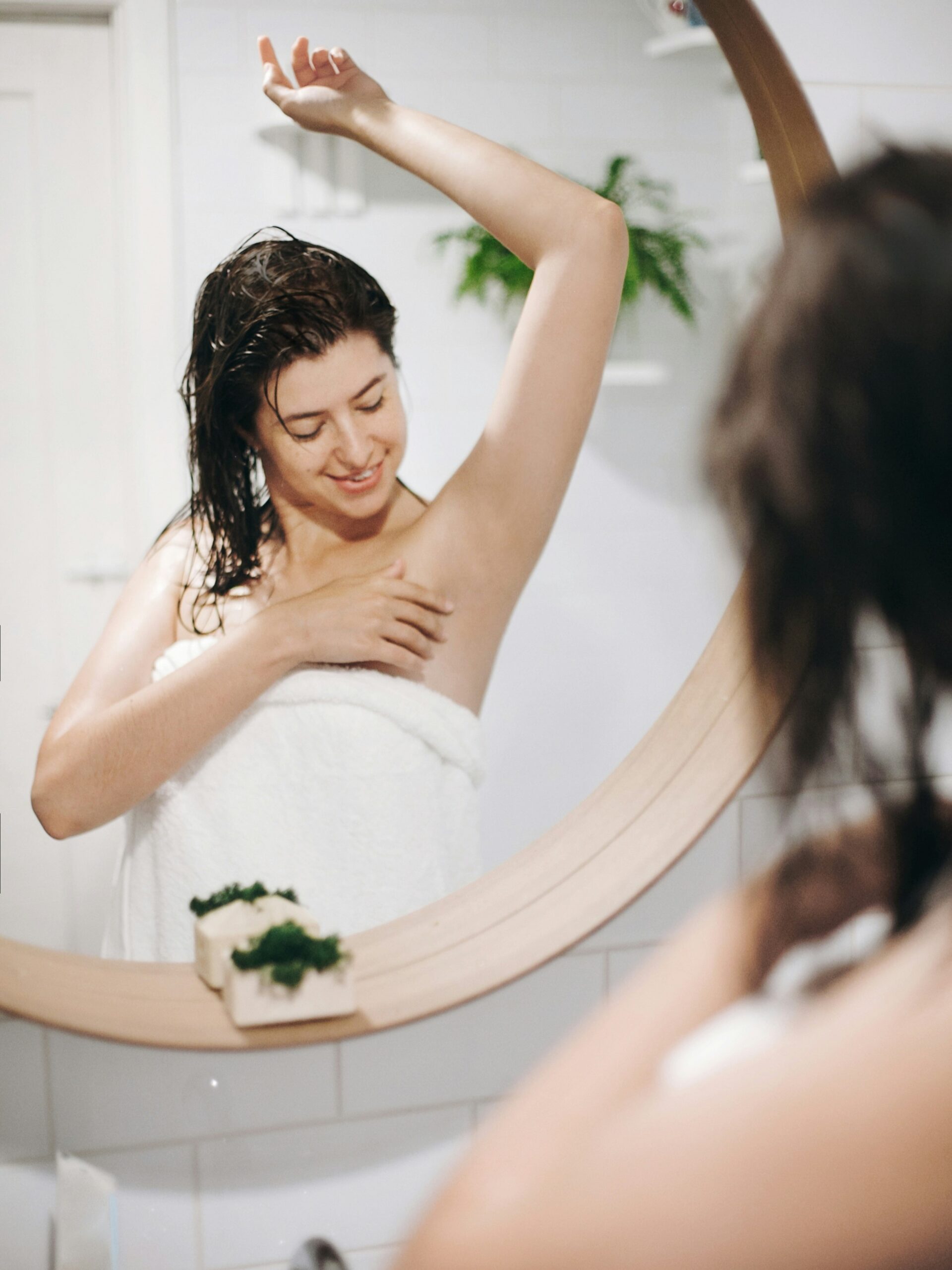 Femme en serviette de bain admirant ses aisselles lisses dans le miroir après une séance d’IPL