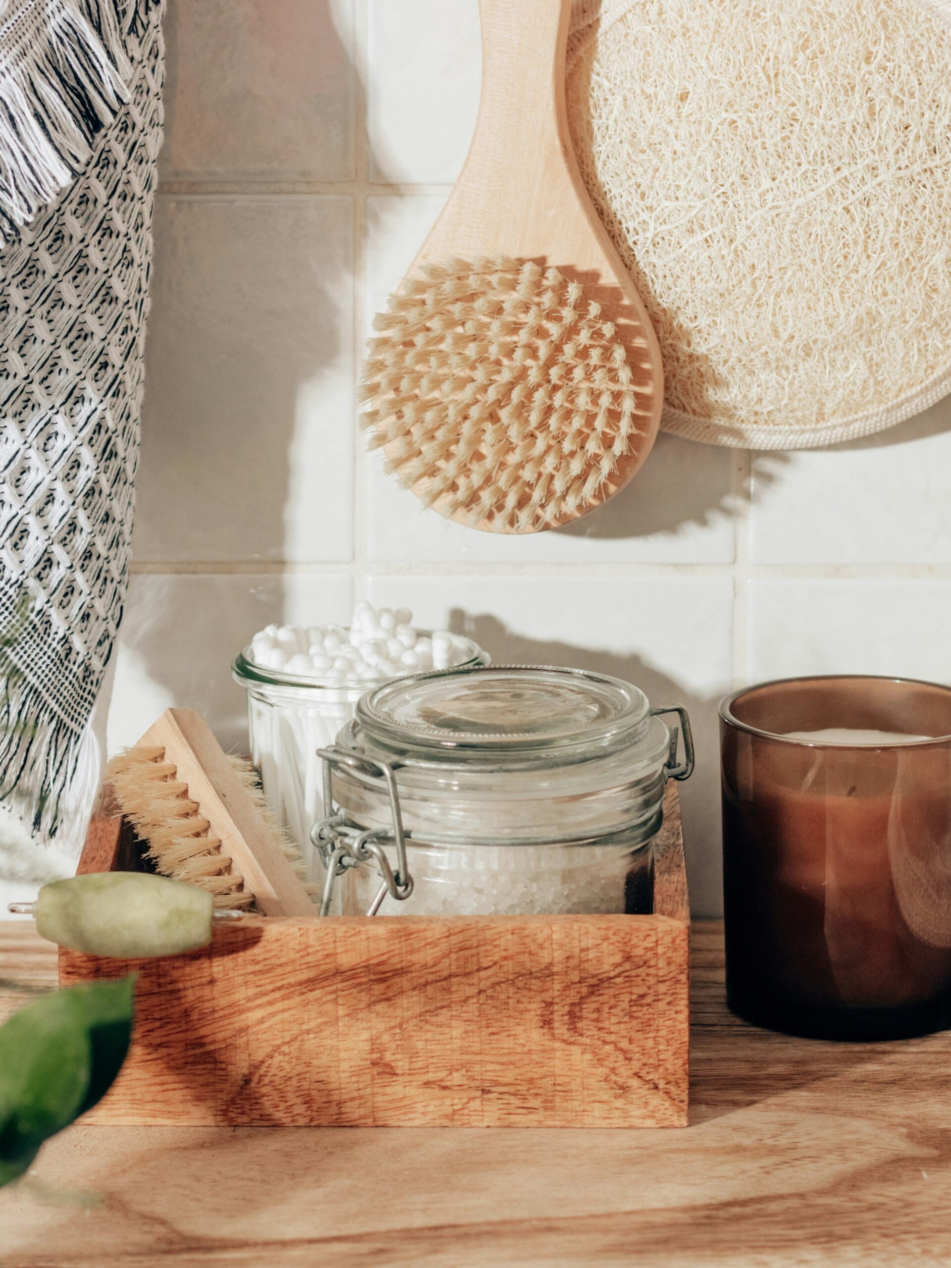 Mise en scène d’accessoires de salle de bain : gant exfoliant, brosse pour le corps, sels de bain, cotons-tiges et bougie