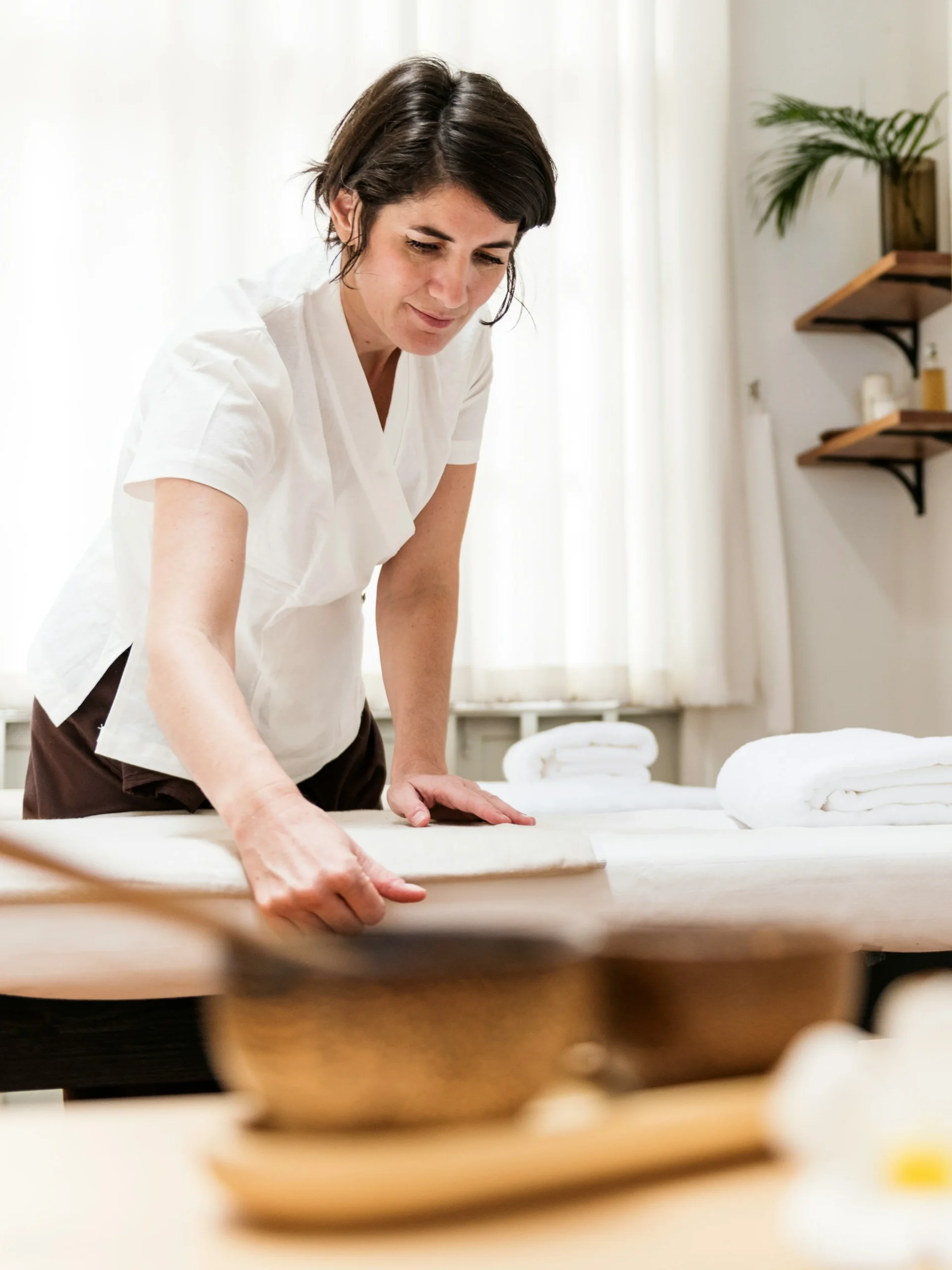 Un réflexologue prépare la salle de soin et lisse le drap de la table, des fleurs et une bougie au premier plan