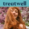 Portrait en gros plan d'une jeune femme rousse souriante avec une frange, dont les cheveux bougent au vent devant un arrière-plan de fleurs de lilas roses. Un bandeau bleu clair en haut affiche le logo "Treatwell" en bleu foncé.