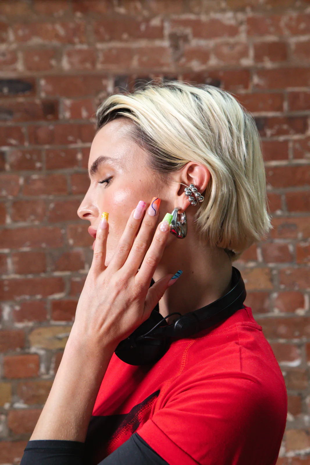 La DJ et actrice Rex Adams de profil, le casque autour du cou, montrant les french tips fluo de la colorée electric mani