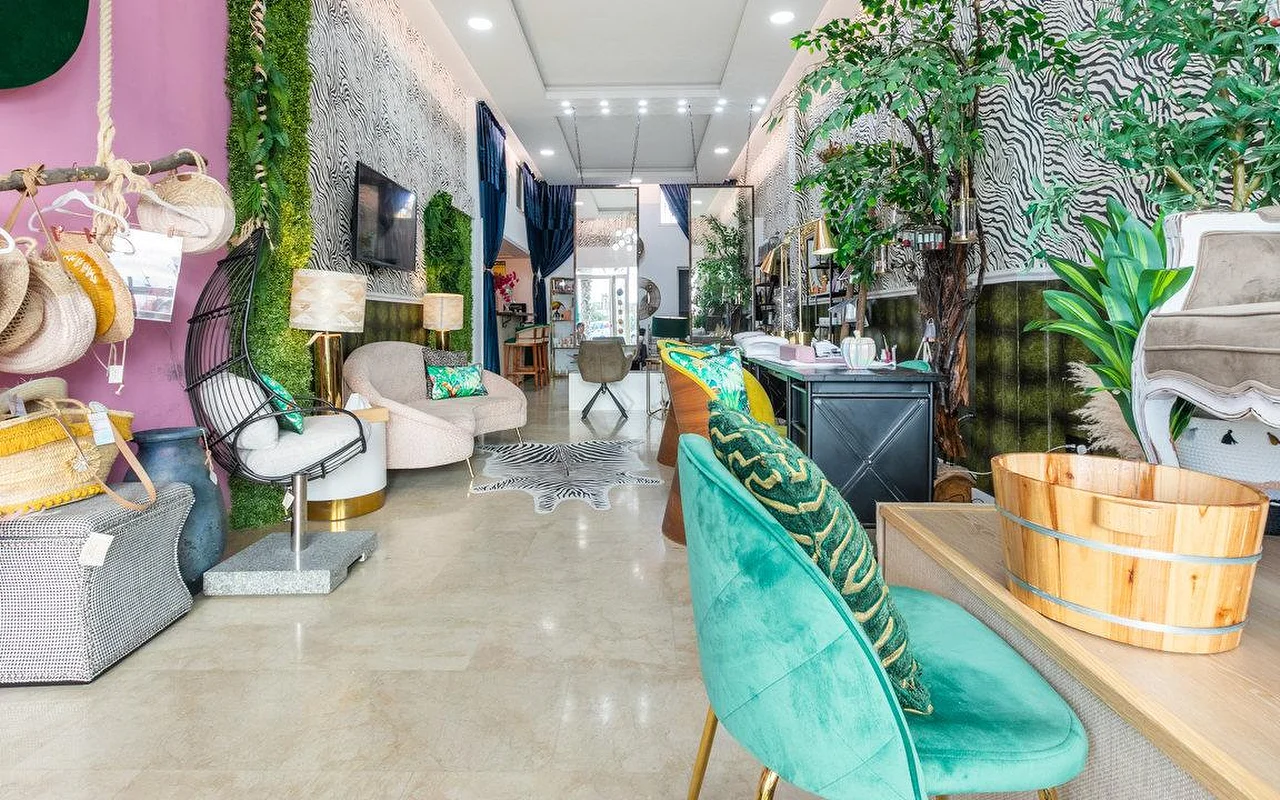 L'intérieur de Brazilian Beauty Marbella, un salon lumineux aux murs à imprimé zèbre, un mur végétal, des fauteuils en velours turquoise et un bac à pédicure en bois.