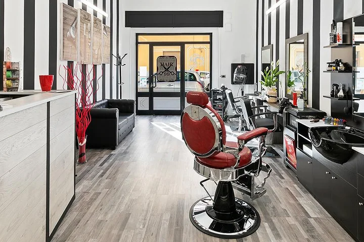 Fauteuil de barbier rouge vintage chez Hair 99 à Alghero, avec ses murs à rayures noires et blanches emblématiques.