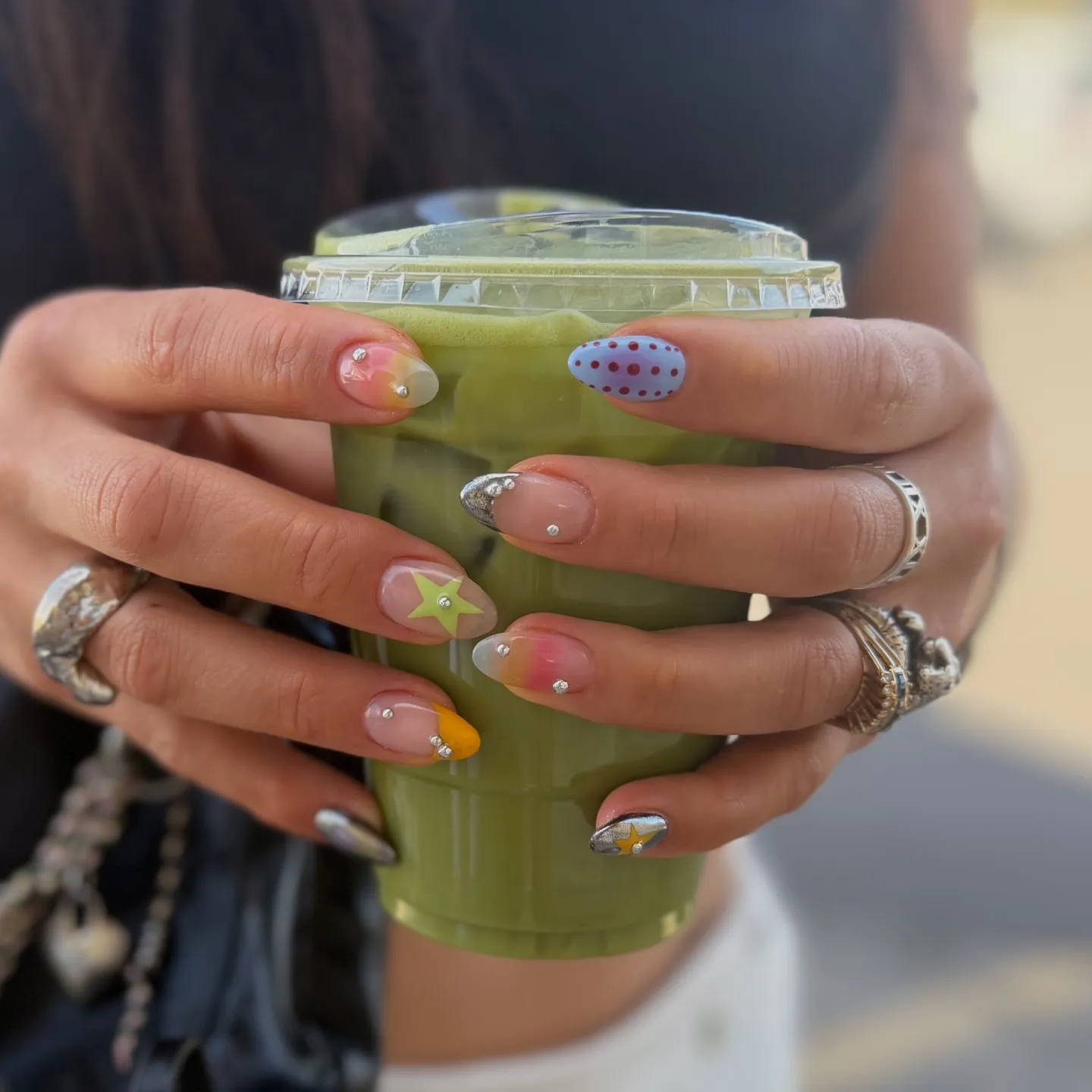 Ensemble de nail art varié avec de petits piercings en cristal, des motifs étoile et des touches colorées sur des ongles en forme d'amande