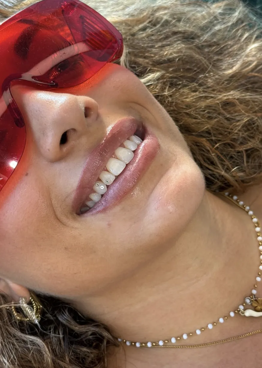 Gros plan sur un sourire dévoilant deux petits bijoux dentaires en cristal sur les dents du bas, portrait estival