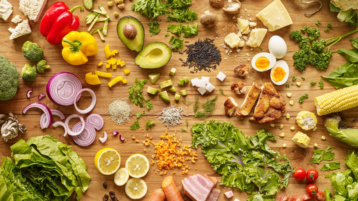 Vue du dessus d'un plan de travail en bois couvert d'aliments nutritifs et colorés, avec œufs, légumes, salade et poulet