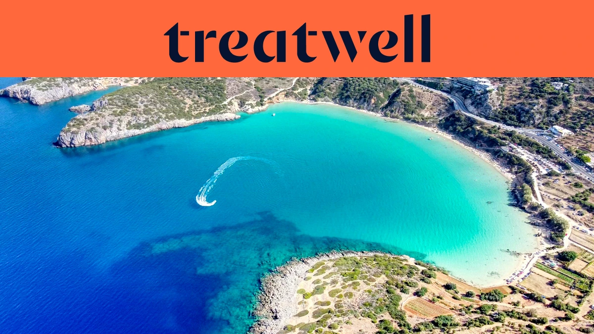 Vue aérienne d'une baie crétoise turquoise, avec un jet-ski traçant une courbe blanche dans l'eau claire, un croissant de plage de sable et des collines sèches autour du rivage, sous une bannière orange corail portant l'inscription treatwell.