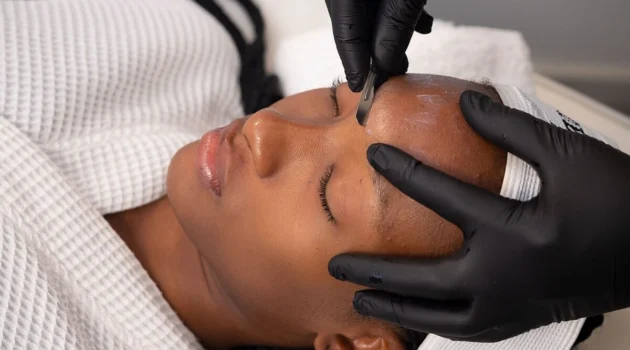 Gros plan d'une esthéticienne réalisant un dermaplaning sur une cliente en institut