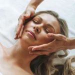 Femme détendue pendant un drainage lymphatique du visage, les mains du praticien glissant délicatement sur ses joues