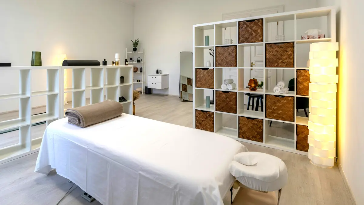 Cabine de soin propre et bien rangée dans un institut, avec une table de massage habillée de draps et une couverture roulée, prête pour un massage